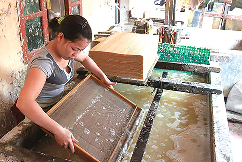 A woman pulling a sheet of Dó paper from the vat on a wooden frame over water